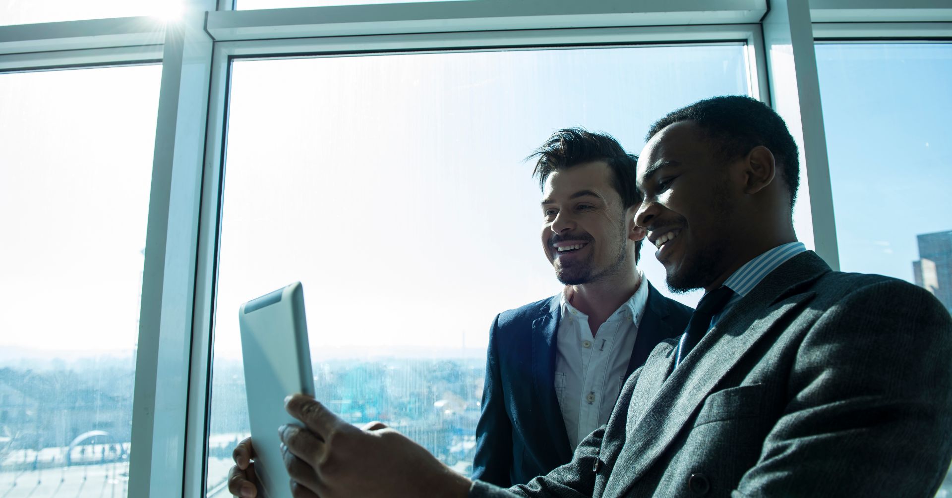 two men in suits looking at an ipad